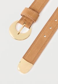 Ταν σουέτ ζώνη με χρυσό κυκλικό κούμπωμα και χρυσό άκρο. Διαθέτει ραφές κατά μήκος της ζώνης και πολλαπλές τρύπες ρύθμισης.