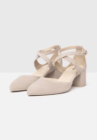 Beige suede high-heeled shoes with a pointed toe, ankle straps, and a block heel. The straps cross over the foot for support.