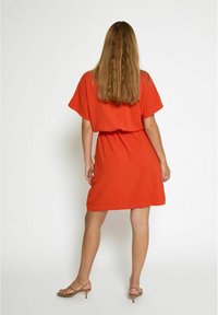 Red short dress with a loose fit, wide sleeves, and a cinched waist. Smooth, lightweight fabric with a knee-length hem.