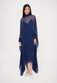 Rochie maxi transparentă bleumarin, cu guler înalt, mâneci lungi și tiv asimetric. Prezintă o textură fluidă și material ușor. Croială conică pe dedesubt.