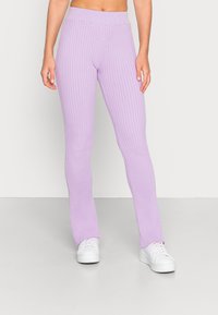 Leggings lavanda com canelado e uma cintura larga, apresentando um silhueta ajustada e bainha levemente evasé, combinados com ténis brancos.