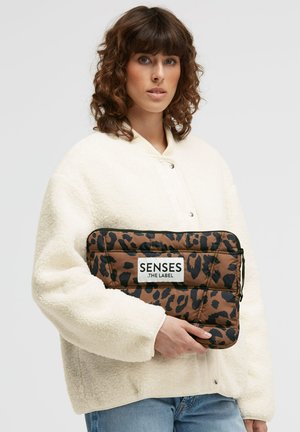 Brown puffer clutch with black leopard print, held against a white fleece jacket. Features a white label with "SENSES .THE LABEL" text.