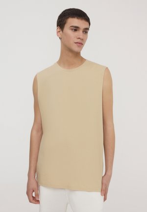 Camicetta beige senza maniche realizzata in morbido cotone, caratterizzata da un collo rotondo e una vestibilità rilassata. Texture liscia con orlo dritto, senza motivi visibili.