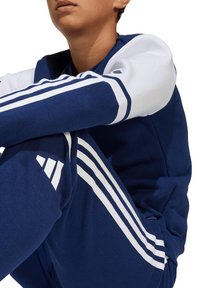 Navy sweatshirt en broekset gemaakt van een katoenmix, met witte strepen langs de mouwen en benen, met een logo ontwerp op de kleding.