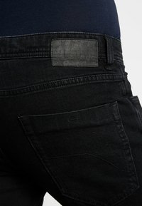 Mustat denimfarkut, joissa on teksturoitu musta nahkainen vyötärönauhan kappale, takatasku, jossa tikattu ääriviiva ja tummat ompeleet.