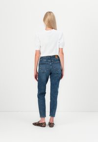 Jeans de mezclilla azul de cintura alta con una textura ligeramente desgastada, combinados con una blusa blanca de mangas abullonadas y unos zapatos planos de estampado de leopardo.