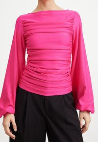 Tajta rosa topp med långa, puffiga ärmar och samlad textur över midjan. Materialet verkar slätt och stretchigt, med en båtringning.