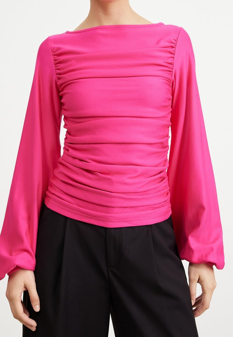 Tajta rosa topp med långa, puffiga ärmar och samlad textur över midjan. Materialet verkar slätt och stretchigt, med en båtringning.
