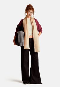 Sweatshirt surdimensionné marron, top court blanc, écharpe beige, pantalon large noir, pull gris, sac noir, textures lisses, palette de couleurs neutres.