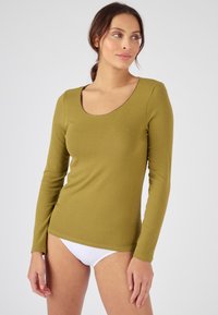 Top de manga larga verde olivo hecho de una tela suave, con un escote redondeado y un ajuste ceñido, combinado con un brief blanco.