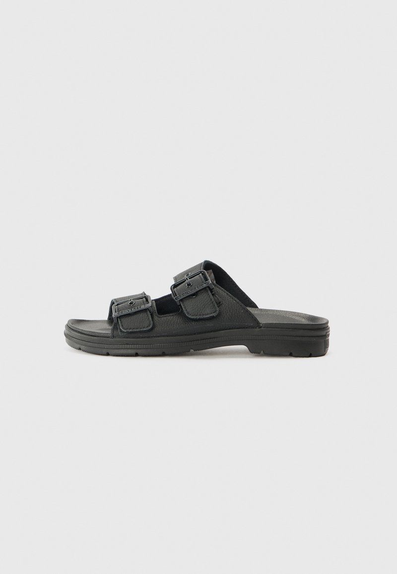 Black slide sandals made of textured synthetic material, featuring two adjustable straps with metal accents and a flexible rubber sole.