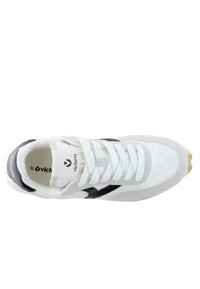 Zapatilla atlética blanca y negra con un exterior de cuero suave y gamuza, punta redonda, cordones planos y una suela de goma con agarre texturizado.