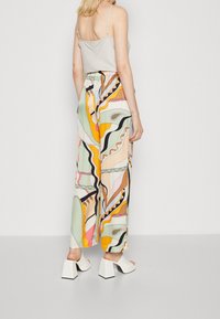 Ljusgrå spaghetti-strap topp parat med lösa, mönstrade vida byxor i pastellfärger, med abstrakta mönster. Vita mules med fyrkantig klack.