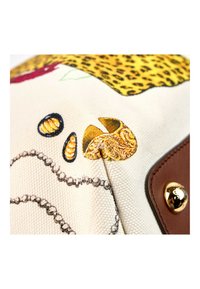 Gros plan d’une surface en tissu avec des coquillages imprimés, un collier de perles, un motif léopard et un coin en cuir marron avec un bouton doré.