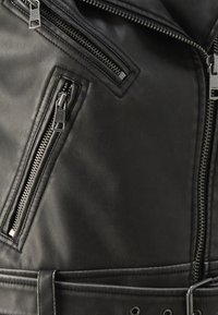 Svart läderjacka med flera dragkedjefickor, detaljerad sömnad och en figurnära design med accenter vid axlarna och midjan.