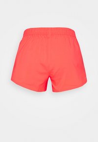Pantalones cortos deportivos elásticos de color coral brillante, mostrados desde atrás sobre un fondo claro y liso.