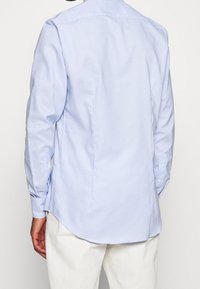 Hellblau kariertes Langarmhemd aus Baumwolle mit abgerundetem Saum, knöpfbaren Manschetten und einer Rückenpasse für Struktur und Passform.