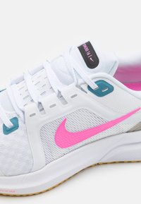 Scarpa sportiva bianca con accenti rosa e aqua, tomaia in rete testurizzata, lacci e suola in gomma. Presenta un logo Nike pronunciatamente rosa.
