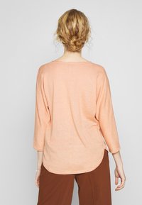 Top lungo a maniche lunghe color pesca chiaro con scollatura a barca, vestibilità rilassata e orlo arrotondato. Tessuto morbido con leggera texture e spacco laterale.