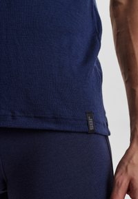 Navy blue fitted t-shirt made of soft fabric with a subtle texture. Features a small black tag with white logo at the hemline.