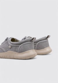 Chaussures en daim gris avec une semelle en caoutchouc beige, de forme arrondie et avec des accents cousus. Elles présentent une petite étiquette sur le talon et un col rembourré.
