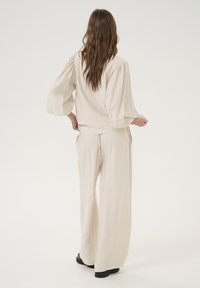 Beige crinkled fabric top with puff sleeves, paired with wide-leg pants featuring a subtle textured pattern, worn with black footwear.