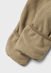 Beiga fleecevantar med mjuk textur och bruna kantdetaljer, överlappande mot en vit bakgrund.