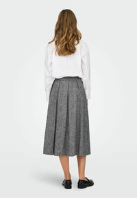 Pelēka krokota svārki ar teksturētu audumu, apvienoti ar baltu krekliņu ar pogām. Tērpam ir augsta josta un teļiem līdzīga garuma dizains.