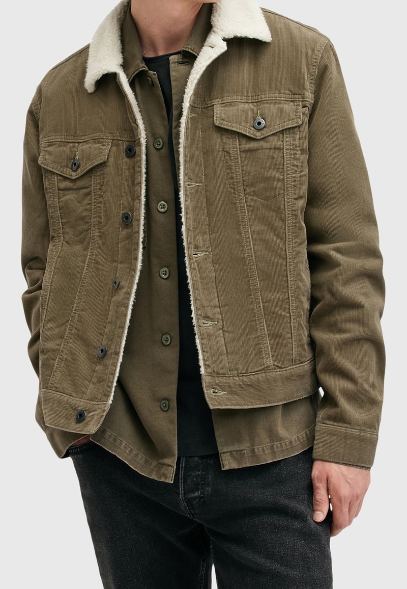 Veste en velours côtelé vert olive avec un col en shearling crème, dotée de poches à boutons, d'une fermeture à boutons sur le devant et de détails en tissu texturé.