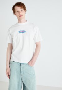 Tricou alb din bumbac, cu un design grafic colorat pe piept. Modelul îl asortează cu șorturi din denim de un albastru deschis.