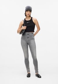 Čierny rebrovaný crop top, šedé nohavice s vysokým pásom, čierne mokasíny, šedá čiapka, malá čierna taška, minimalistický dizajn, priliehavý silueta.