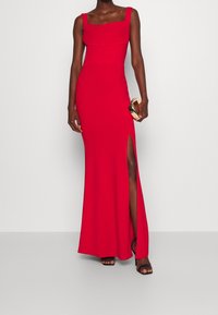 Robe de soirée rouge avec un décolleté carré, un corsage ajusté et une fente latérale haute jusqu'à la cuisse. Tissu lisse et design minimaliste. Accompagnée d'une pochette.