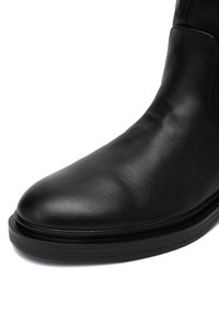 Czarne skórzane botki o gładkiej fakturze, zaokrąglonym nosku, niskiej gumowej podeszwie z rowkami oraz minimalnym detalowaniu szwów.