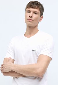 White cotton t-shirt with short sleeves. Features a small green "BOSS" logo on the left chest area. Smooth texture, classic crew neck design.