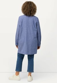 Camicia lunga a righe blu e bianche, con colletto e polsini a bottone, abbinata a jeans blu cropped e sneakers bianche. Materiale in misto cotone.