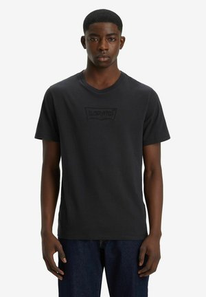 T-shirt en coton noir avec un col rond et des manches courtes, arborant un logo Levi's en relief sur la poitrine. Coupe classique et texture douce.
