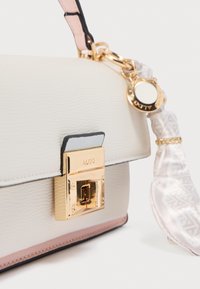 Sac à main en similicuir crème texturé avec une fermeture à boucle dorée, des accents roses, un détail d'écharpe à motif et une bordure noire.