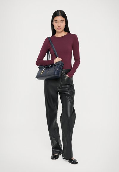 Bordeauxfarbener langärmeliger Oberteil, schwarze Kunstleder-Hose mit weitem Bein und marinefarbene Handtasche mit einem Schlüssel-Detail, die über eine glatte Textur und eine strukturierte Form verfügt.