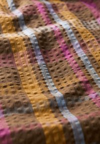 Texturovaná tkanina s teplými hnědými, žlutými a růžovými pruhy. Povrch má vyvýšenou, vzorovanou texturu, která zvyšuje vizuální zajímavost.