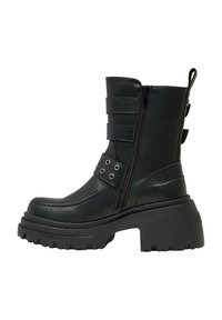 Botín de cuero negro hasta el tobillo con una plataforma gruesa, cierre lateral y correas decorativas con acentos de metal. Suela estriada para mayor tracción.