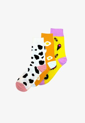 Trois paires de chaussettes en coton : une blanche avec des pois noirs, une orange avec un motif d'œuf au plat jaune, et une jaune avec des motifs de glace et de bonbons.