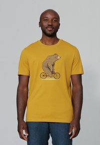 Geel katoenen T-shirt met als centraal gedrukt ontwerp een beer die op een fiets rijdt. Korte mouwen en een ronde hals.