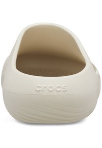 Kremfarbene Crocs mit einer strukturierten Oberfläche, offenem Hinterdesign und einem erhöhten "crocs"-Logo. Die Innenseite verfügt über eine glatte, gepolsterte Oberfläche.