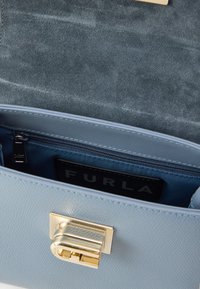 Hele sinine nahast käekott tekstureeritud viimistlusega, kuldse kinnitusdetailiga ja sinise sisevoodriga, mis sisaldab lukuga taskut.