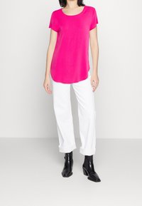 Haut fuchsia à manches courtes avec encolure ronde, ourlet légèrement arrondi, associé à un pantalon blanc retroussé et des bottines noires.