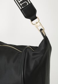 Sac à main en nylon noir avec un accent de fermeture éclair doré et une bandoulière rayée détachable avec un attachement en cuir noir.