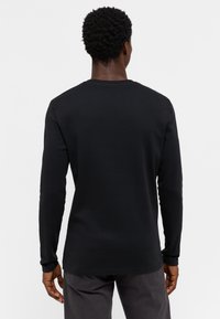 Camiseta de manga larga negra en tela suave y lisosa con cuello redondo y diseño ajustado. Presenta puños acanalados y un dobladillo recto.