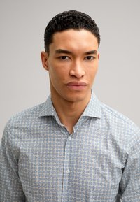 Camicia button-up azzurro chiaro con un motivo geometrico in blu scuro e beige. Presenta un colletto classico e maniche lunghe. Trama liscia.