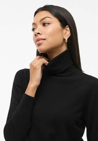 Czarny sweter z golfem, z prążkowanym dekoltem i mankietami. Miękka tekstura, dopasowany krój i minimalistyczny design.