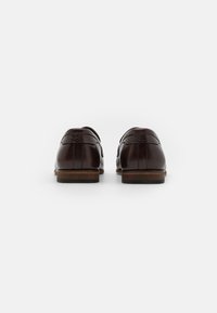 Zapatos de cuero marrón con un acabado suave y acentos tejidos. Punta redondeada, tacón bajo y suela resistente, vistos desde atrás.